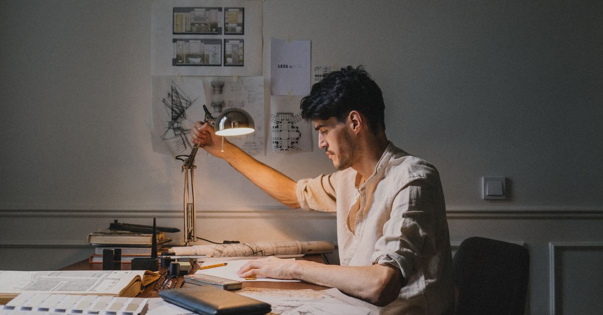 An architect sketching a floor plan at a drafting table surrounded by material samples
