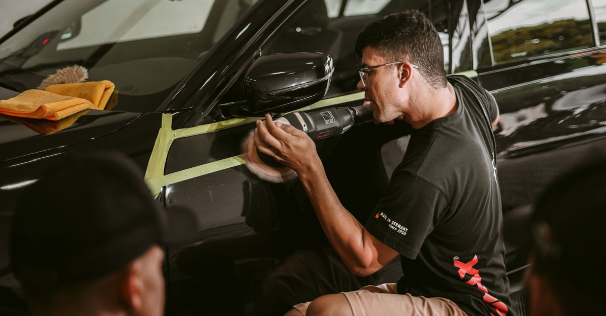 A professional auto detailer polishing the hood of a car in a bright detailing bay