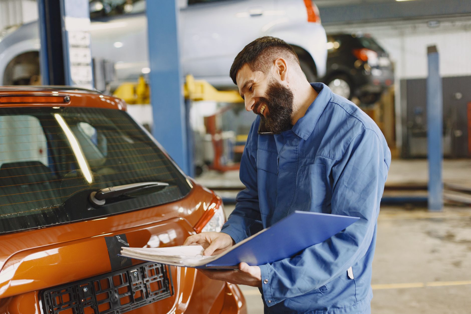 A friendly mechanic with a clipboard inspecting a car in the shop