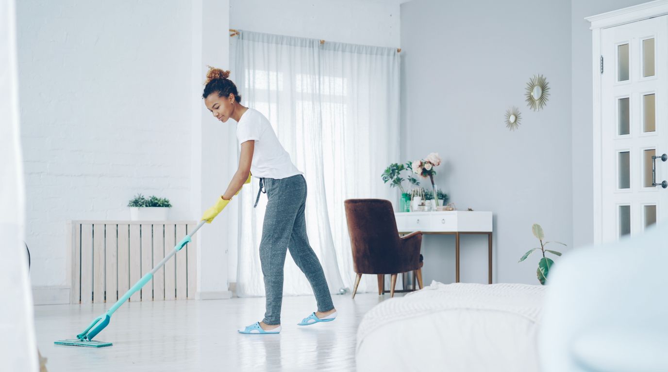 A cleaner mopping the floor of a bright modern living room, too busy on the job to market