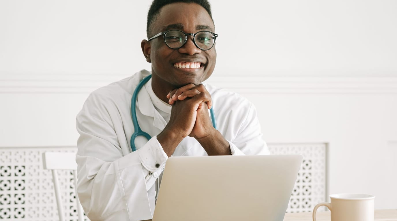 A friendly, confident doctor in a white coat smiling in a bright modern medical office