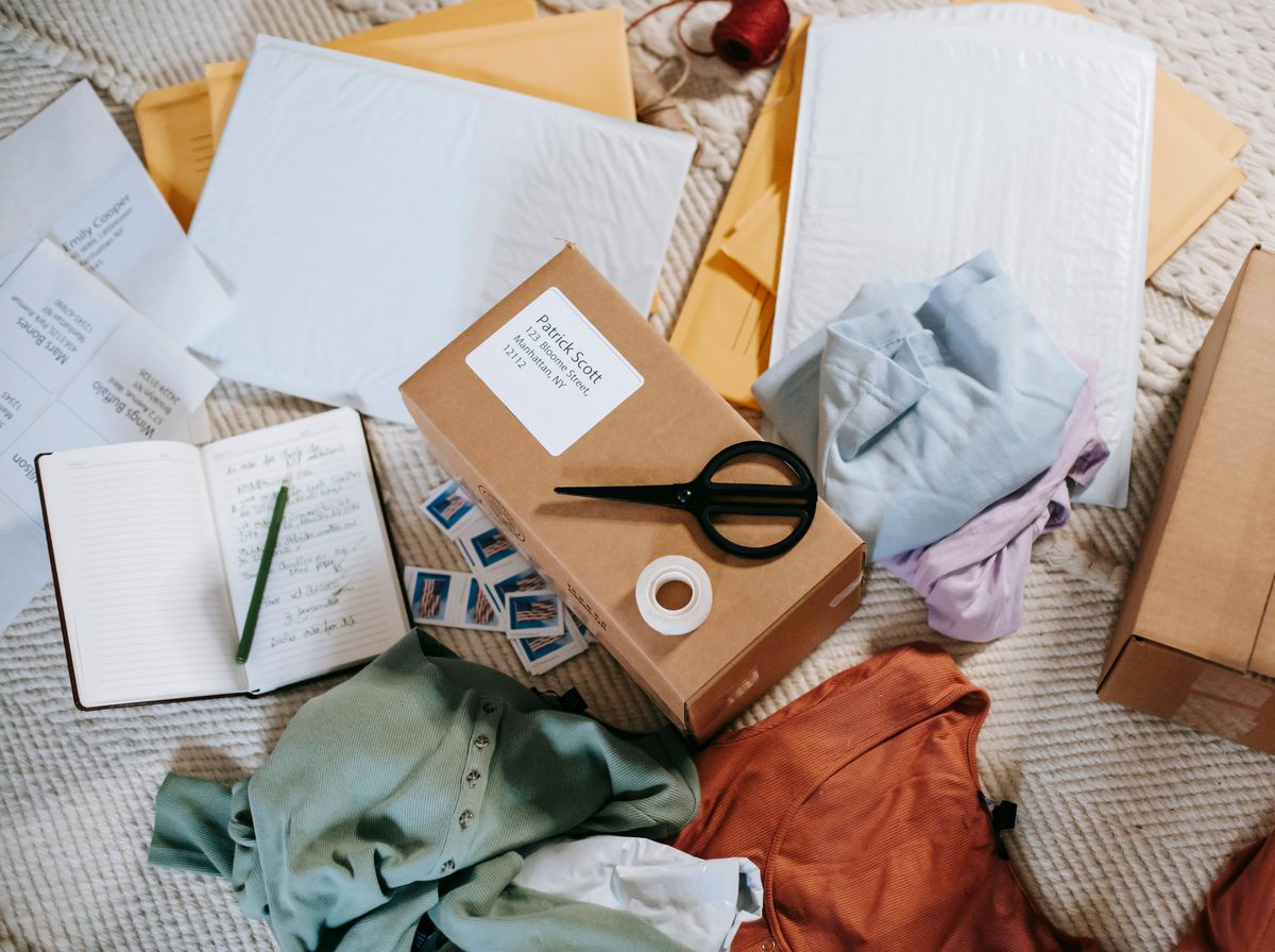 An ecommerce packing station flat lay with mailers, a labeled parcel, folded apparel, and handwritten order notes