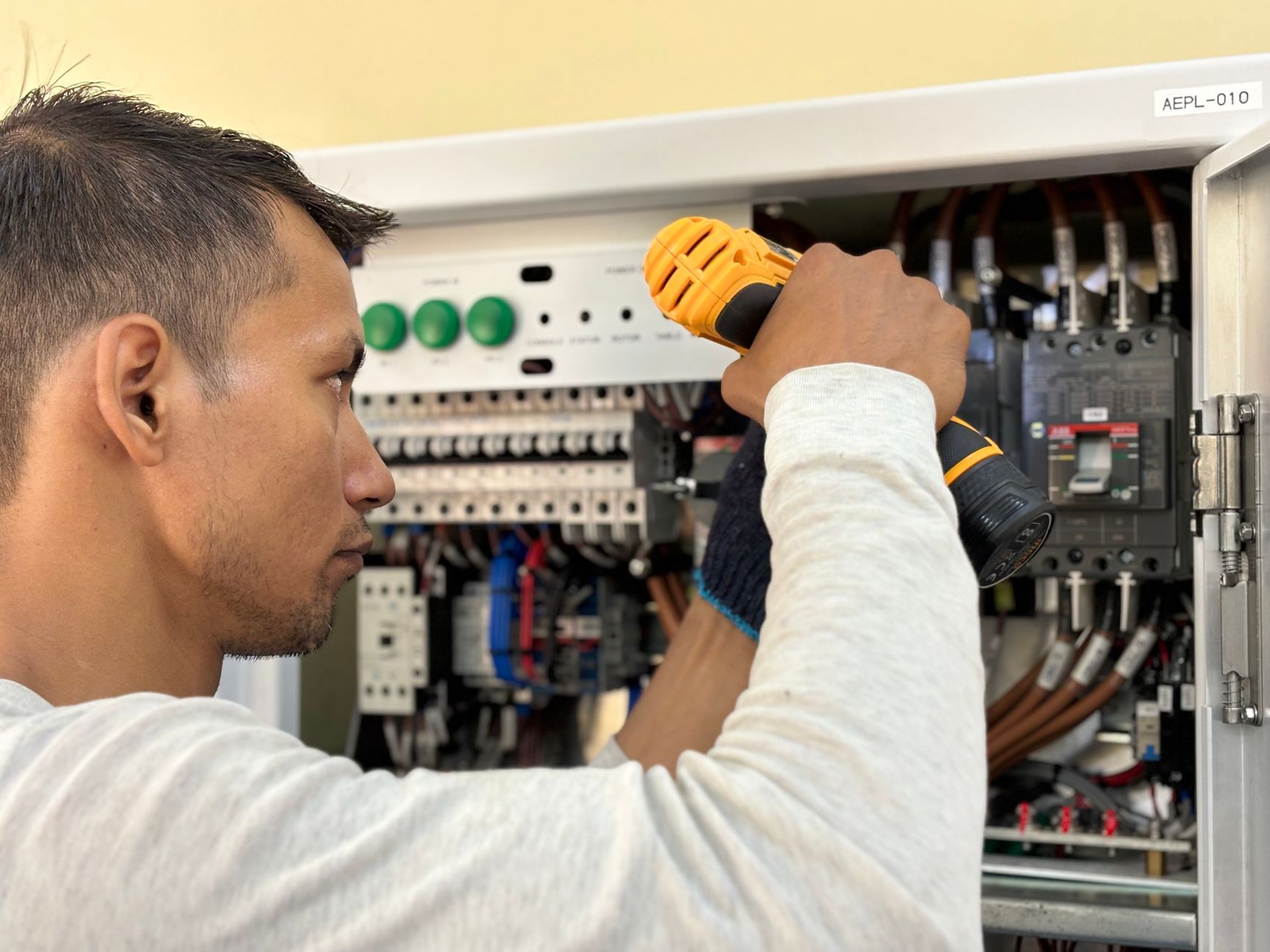 An electrician using a drill on an interior electrical circuit