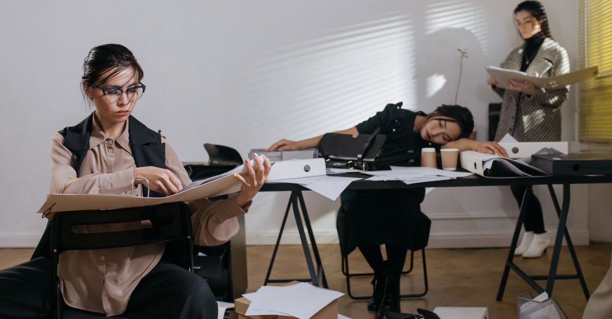 A small nonprofit team buried in paperwork at a cluttered office, stretched too thin to also do marketing