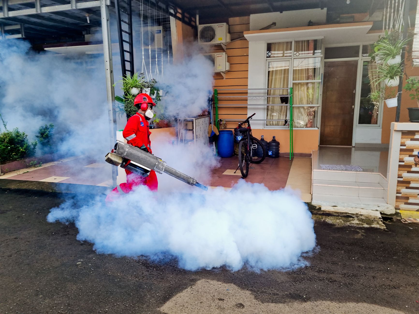 A pest control technician fogging around a home to control mosquitoes and pests