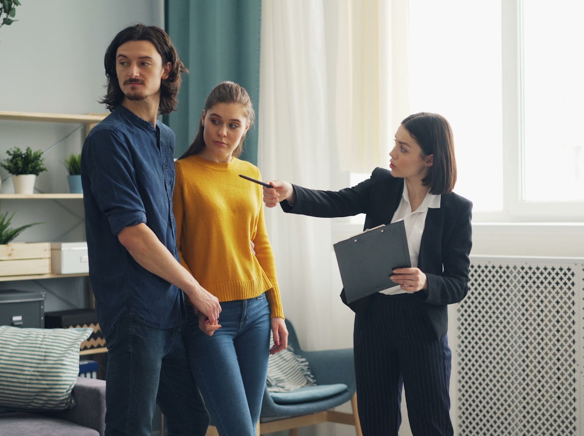 A real estate agent with a clipboard walking a young couple through a home showing