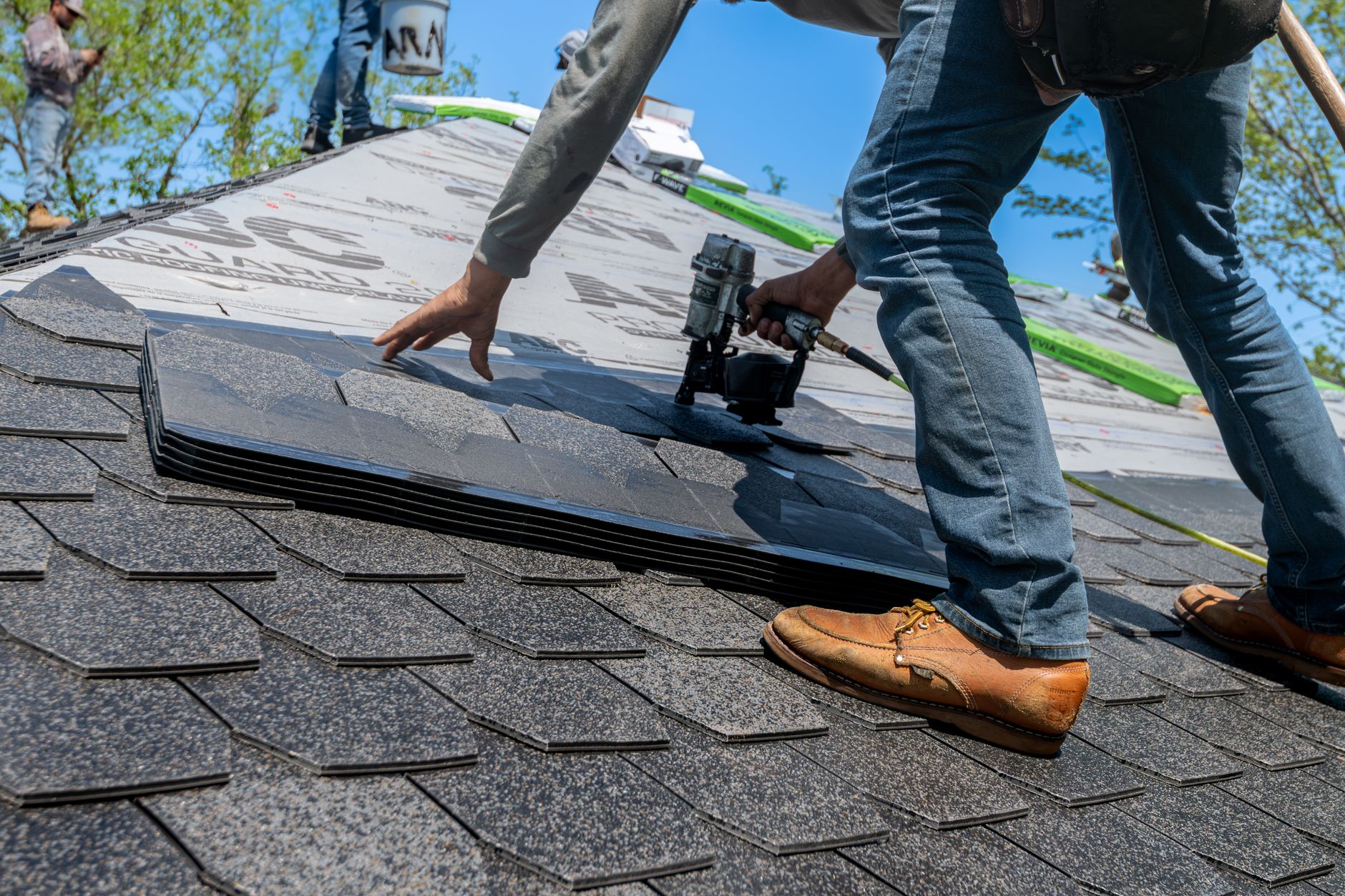 A roofer using a nail gun to install shingles on a residential roof